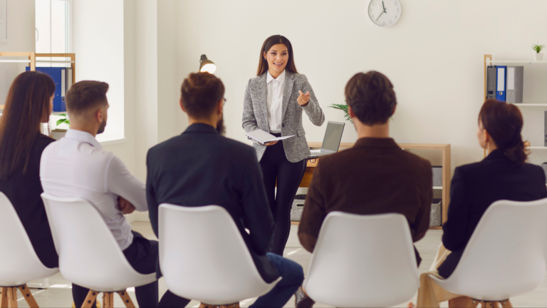 Professional trainer conducting a public speaking and communication workshop for a group in an office setting.