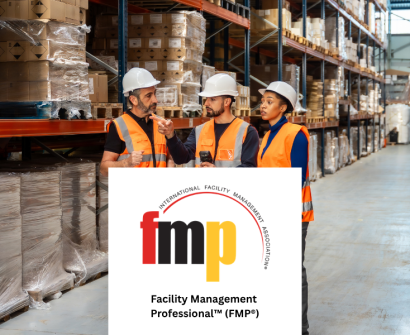 Warehouse facility management professionals wearing safety helmets and orange high-visibility vests discussing operations in a large storage warehouse, with the IFMA Facility Management Professional (FMP) certification logo displayed in the foreground.