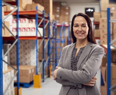 Portrait Of Female Team Leader Standing By Shelves In Warehouse